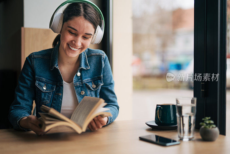 Shot of a young woman listening to music while reading a book